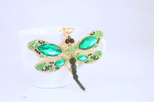 Detail of green crystal dragonfly keychain with gold metal base on a ceramic cup