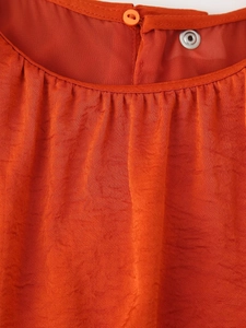 Macro detail of orange sleeveless dress showing pleated neckline and decorative buttons
