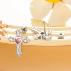 Silver cross stud earrings with pink heart zircon and clear crystal accents on a warm base