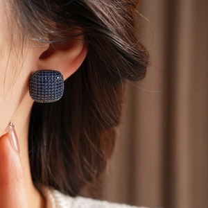 Close-up of vintage square stud earring with dark blue zircon stones on model