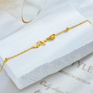 Minimalist gold heart and heartbeat anklet displayed on white stones with soft lighting