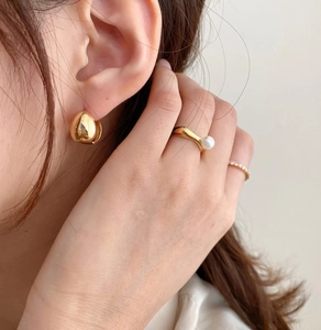 Close-up of golden teardrop earrings and pearl ring set on model with a soft finish