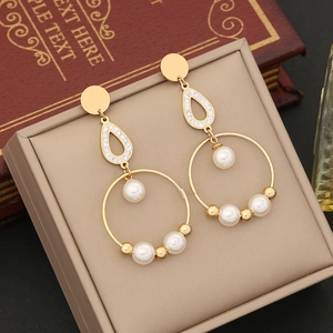 Golden drop earrings with white pearls and zircons placed on a jewelry box edge