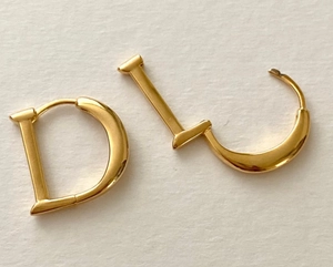 Flat lay macro of polished gold D-shaped letter earrings on a textured background