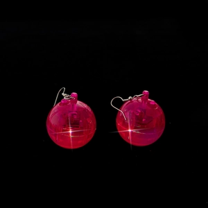 Close-up of pink luminous spherical earrings with silver hooks on black background