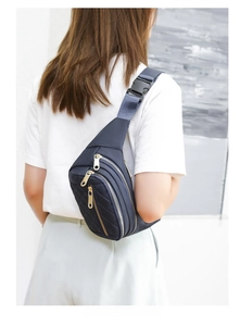 Close-up of navy blue quilted chest bag with triple gold zippers and adjustable strap