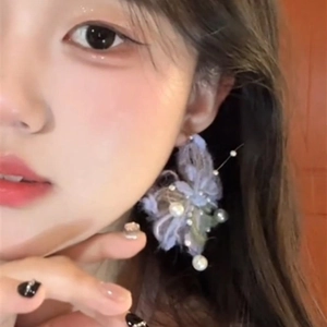 Detail view of purple yarn flower earrings with pearls on model's side profile