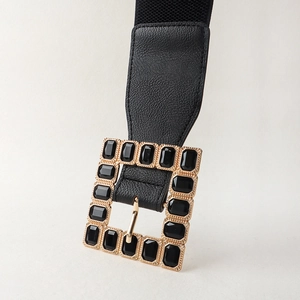 Detail of a square gold buckle with black faceted gems on a 6cm elastic waist belt