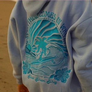 Light blue hoodie with 3D waves and palm tree embroidery and Everything Comes In Waves text
