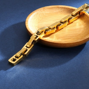 Detail of a golden geometric cuban chain bracelet on a round wooden tray and blue backdrop