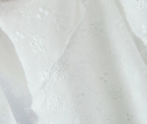 Detailed macro view of delicate white floral embroidery on premium cotton lace fabric