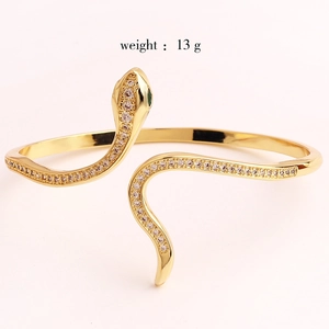 Macro detail of gold snake bracelet featuring white pavé stones and green gem eyes