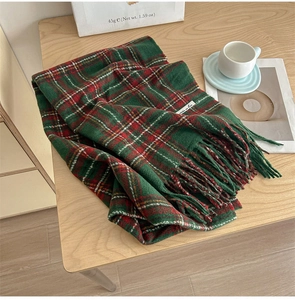 Detail of red and green plaid scarf with soft tassels on a cozy wooden desk setup