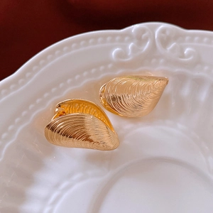 Detailed view of golden shell-shaped earrings with fine texture on a ceramic plate