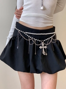 Détail de la chaîne de taille en perles avec pendentif croix en strass sur jupe noire