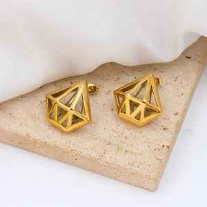 Détail de boucles d'oreilles géométriques dorées en forme de cage sur pierre beige