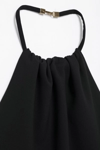 Details des schwarzen Neckholder-Kleids mit plissiertem Stoff und goldenem Metallverschluss