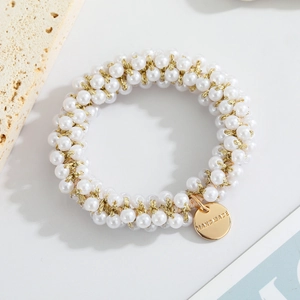Detail of handmade pearl hair tie with gold woven threads and a round metal logo tag