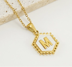 Macro detail of golden hexagonal pendant with letter M on a white marble surface