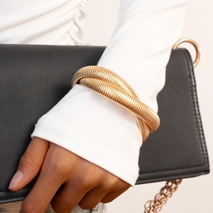 Detailed view of a gold double-layer twisted spiral cuff bracelet worn over a white sleeve