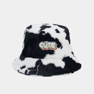 Gros plan d'un bob en peluche à motif vache avec un écusson brodé coloré CUTE