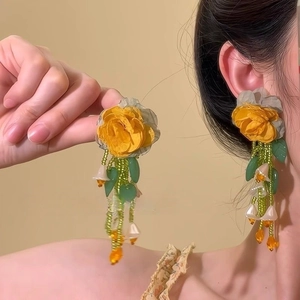Détail de boucles d'oreilles à franges avec fleurs en tissu jaune et pompons verts