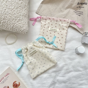 Close-up of floral corduroy drawstring bags with brand labels on a soft linen background