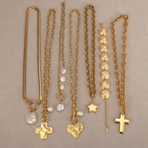 Collares en capas chapados en oro con perlas, cruz y corazón sobre fondo gris mate