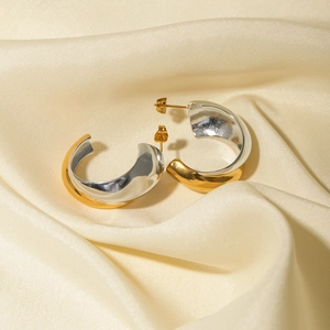 Macro shot of two-tone gold and silver C-shaped earrings on soft beige silk fabric