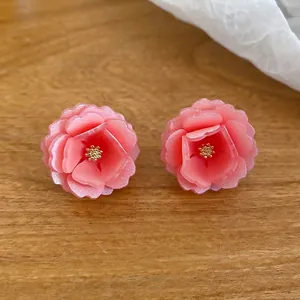 Boucles d'oreilles fleurs roses en résine avec pistils dorés sur fond en bois naturel