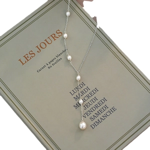 Elegant Y-shaped necklace with white freshwater pearls on silver chain over a book