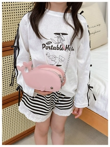 Pink dolphin-shaped child crossbody bag with metallic chain strap shown in a lifestyle setting