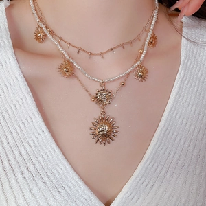 Detail of a layered golden sun pendant necklace with elegant white pearls on model