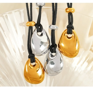 Detail of sleek teardrop pendants on black braided cords over textured glass bowl