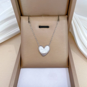 Macro detail of a silver heart necklace with white shell inlay in a golden jewelry box