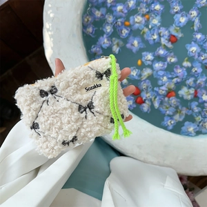 Close-up of white plush cosmetic pouch with black bow embroidery and green drawstring