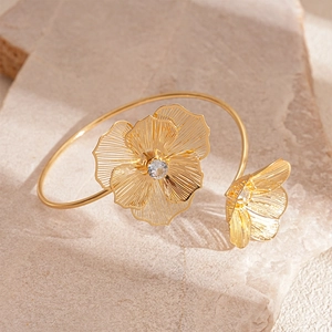 Détail du bracelet doré ajouré avec fleurs en métal et cristaux sur pierre beige