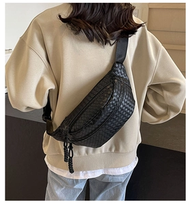 Rear view of a black woven leather crossbody bag worn with a beige hoodie and jeans