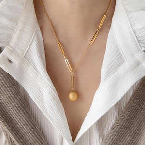 Elegant gold necklace with frosted spherical pendant on layered knit vest and shirt