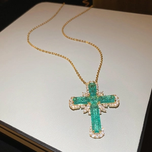 Détail macro du pendentif croix dorée avec pierre verte et accents de micro-cristaux