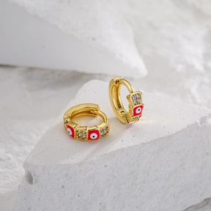 Mini gold huggie earrings with red evil eye pattern and zircon on a textured stone