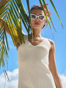 Outdoor shot of a ribbed knit V-neck beige dress with palm leaves against a clear blue sky