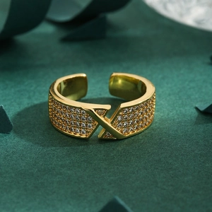 Crossed X-shaped golden open ring with micro-pave crystals on green background