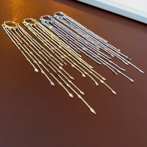 Detail of layered metal chain tassel earrings with leaf charms in gold and silver finish