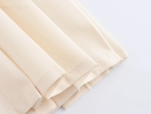 Dettaglio ravvicinato della trama del tessuto bianco crema e cuciture sull'orlo del vestito