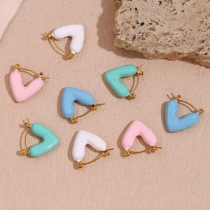 Detail of colorful enamel heart earrings in white, pink, blue and mint on golden hoops