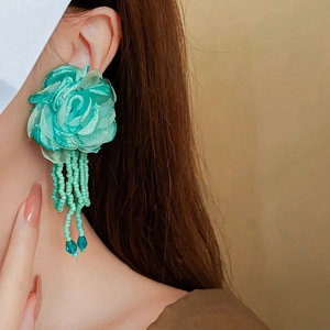 Close-up of mint green fabric flower earrings with long beaded tassels on model