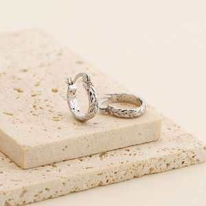 Detail of s925 silver wheat-ear hoop earrings with small gemstones on stone background