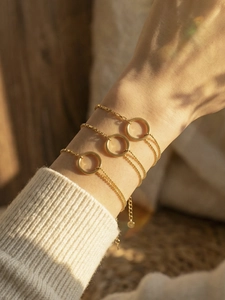 Three-piece gold box and bead chain bracelets with circle pendants on a female wrist