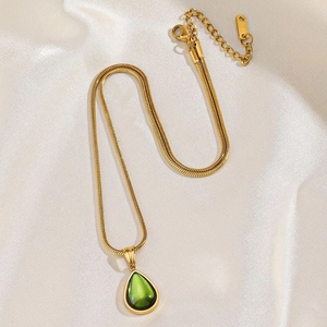 Elegante goldene Schlangenkette mit grünem Tropfenanhänger auf weißer Seide für Damen